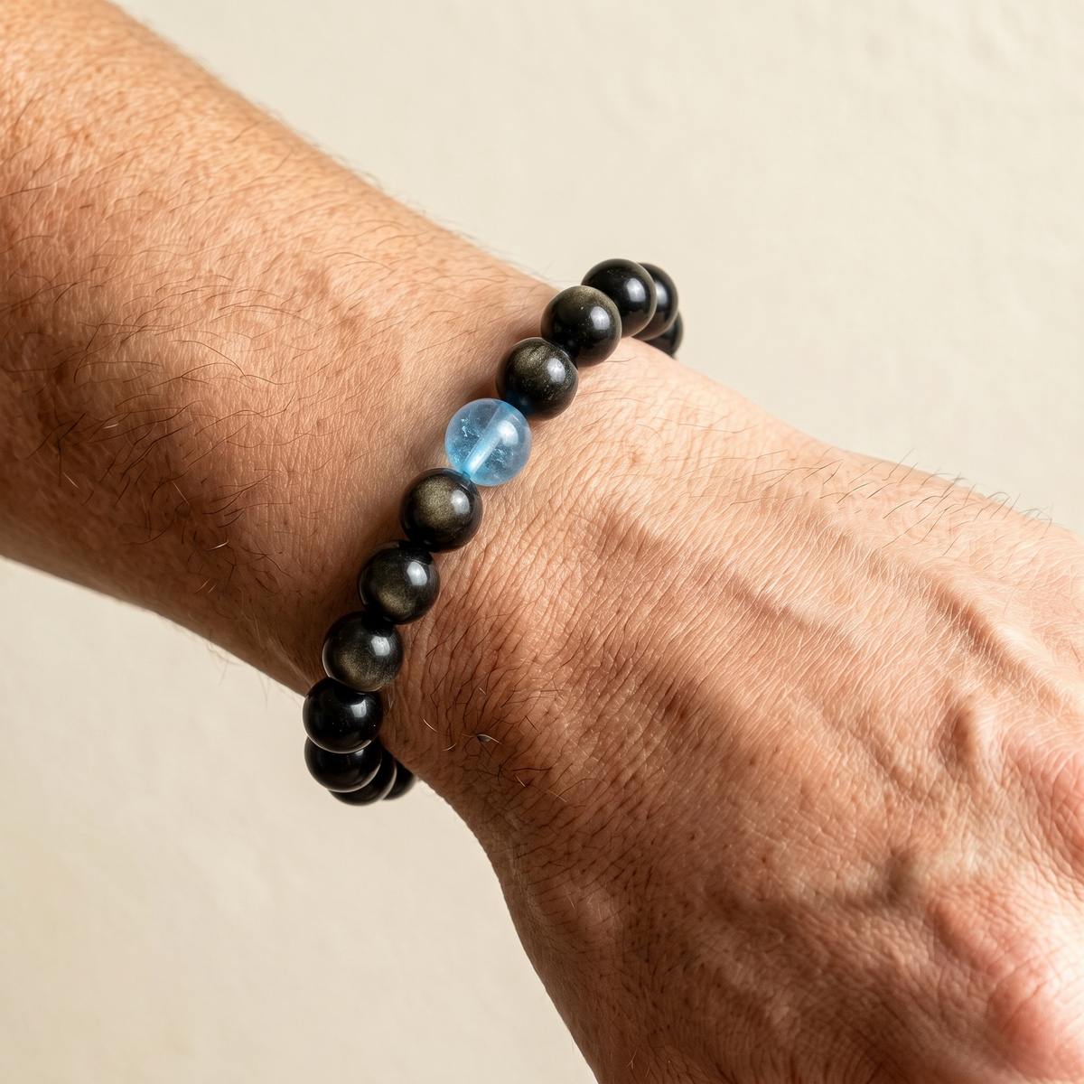 Aqua Sheen on a man's wrist — aquamarine sea-blue and gold sheen obsidian, calm ink tones.