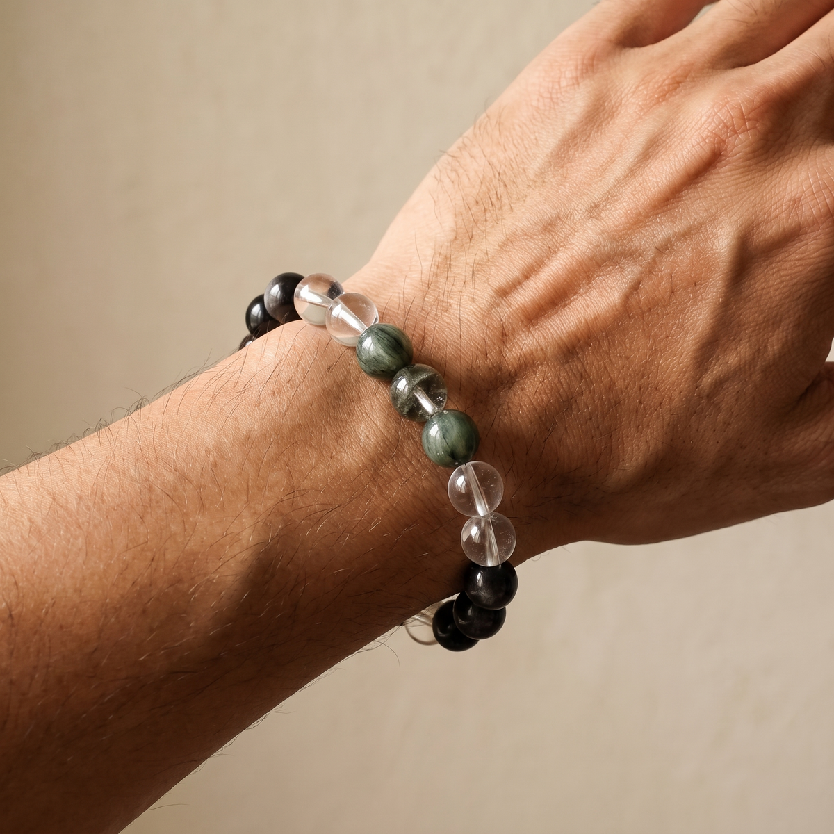Golden Channel bracelet by Krysora worn on a man's wrist - silvery black obsidian with fresh green rutilated and phantom quartz