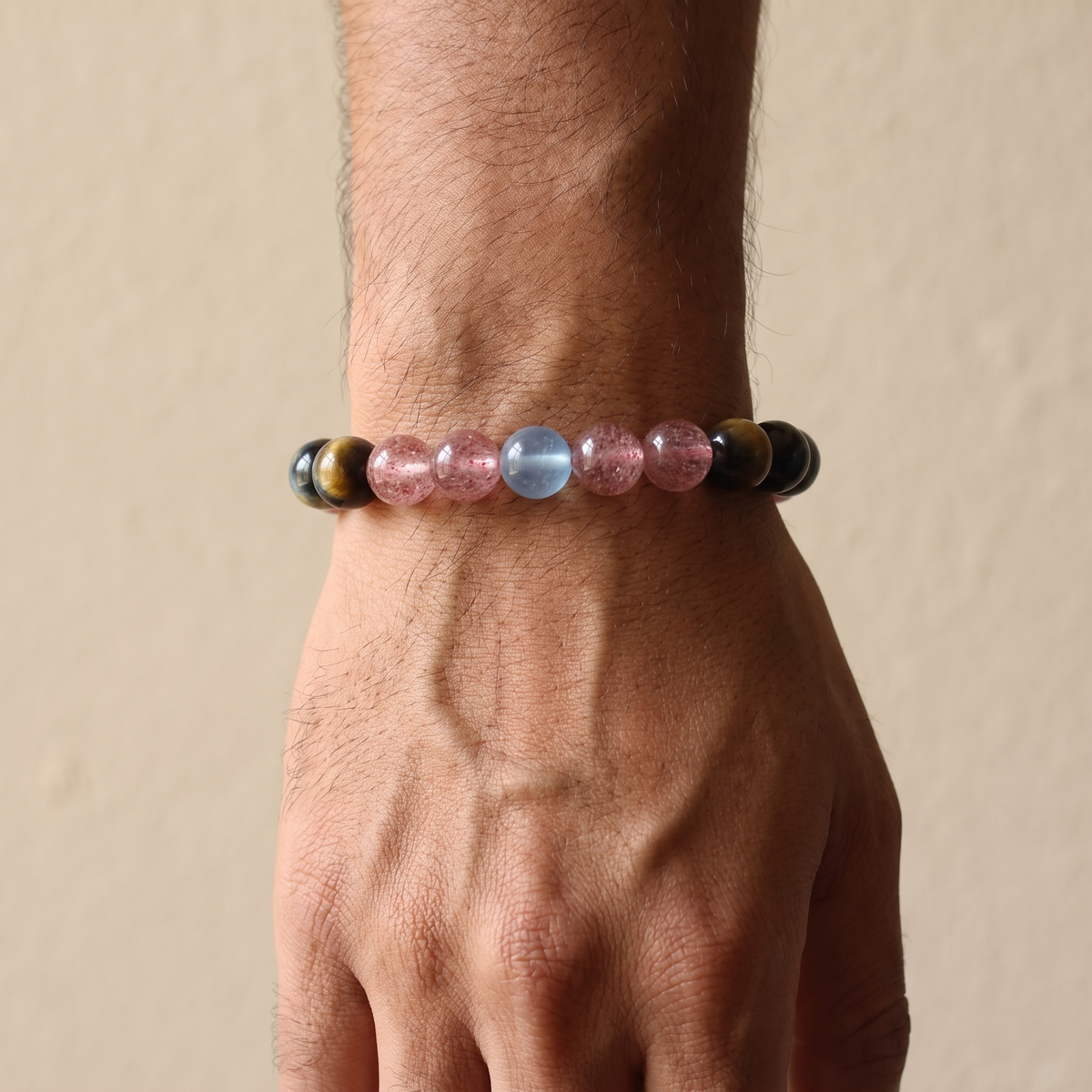 Tri-Sheen bracelet by Krysora worn on a man's wrist - clear blue, warm ochre, and berry-red three-tone gemstones