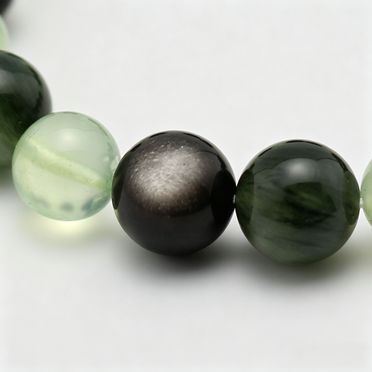 Close-up of the Aqua Verdance bracelet by Krysora - bead detail, silver sheen obsidian, green rutilated quartz, prehnite, ink and sage tones, natural markings